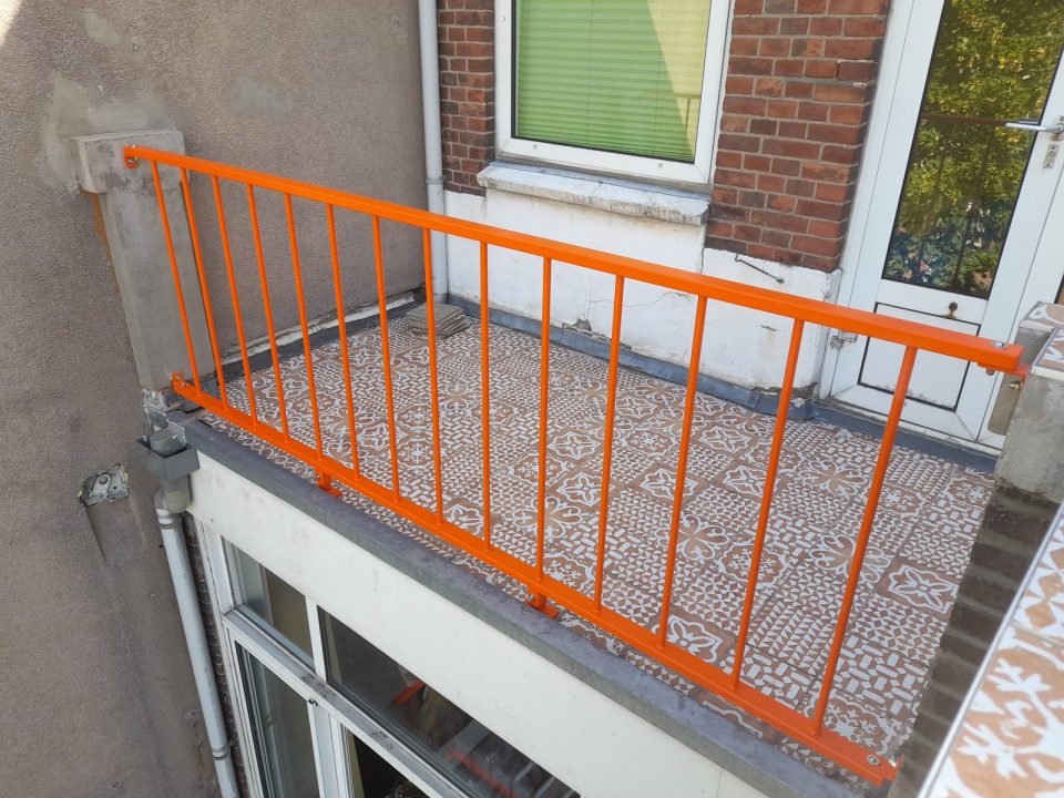Oranje metalen balkonhek met verticale spijlen op betegeld balkon