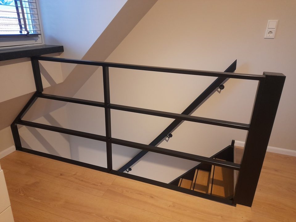Zwarte metalen balustrade rond een trapgat met bijpassende wandleuning